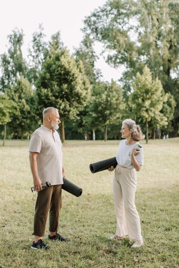 Pareja de adultos mayores con tapetes de ejercicio en jardín